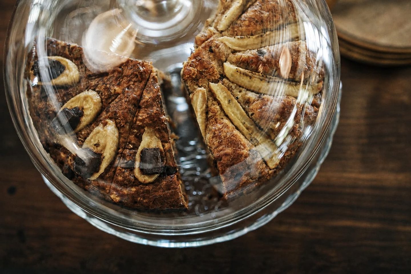 A banana chocolate cake under a glass dome, sliced