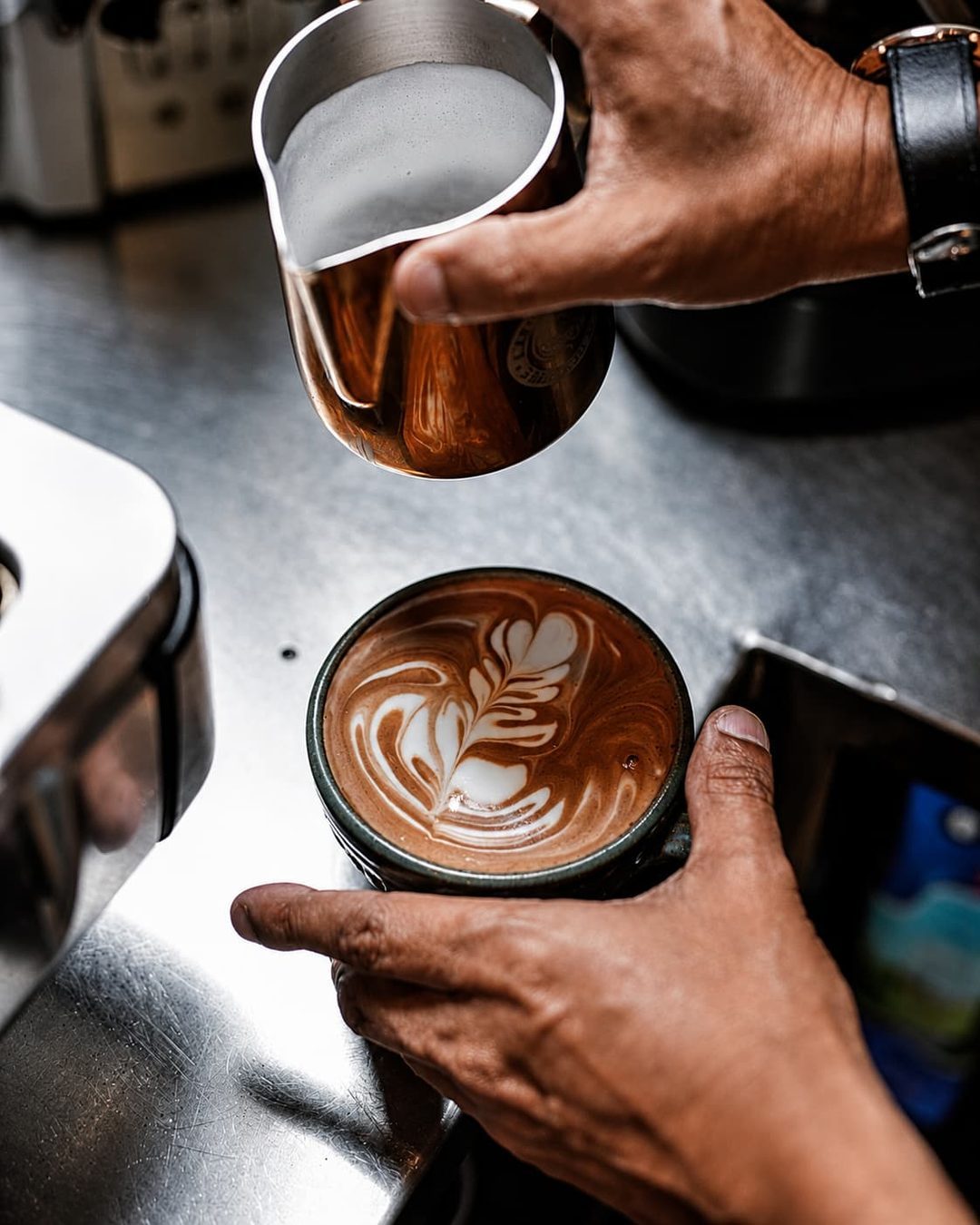 A barista finishing latte art in a dark ceramic cup