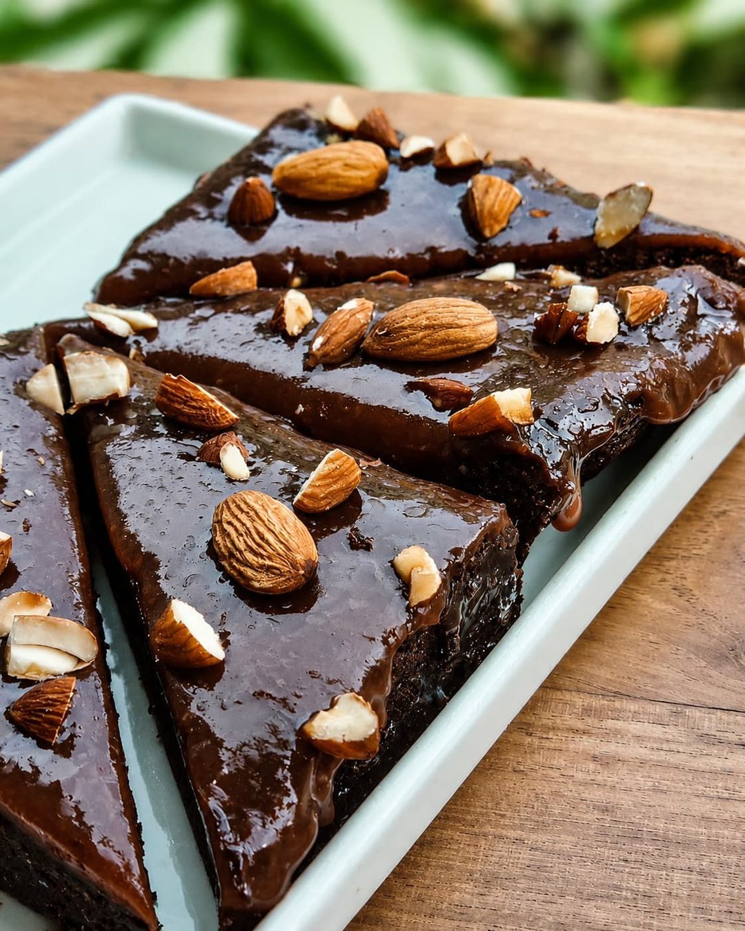 Triangular chocolate brownies with a glossy ganache and toasted almonds on a ceramic tray