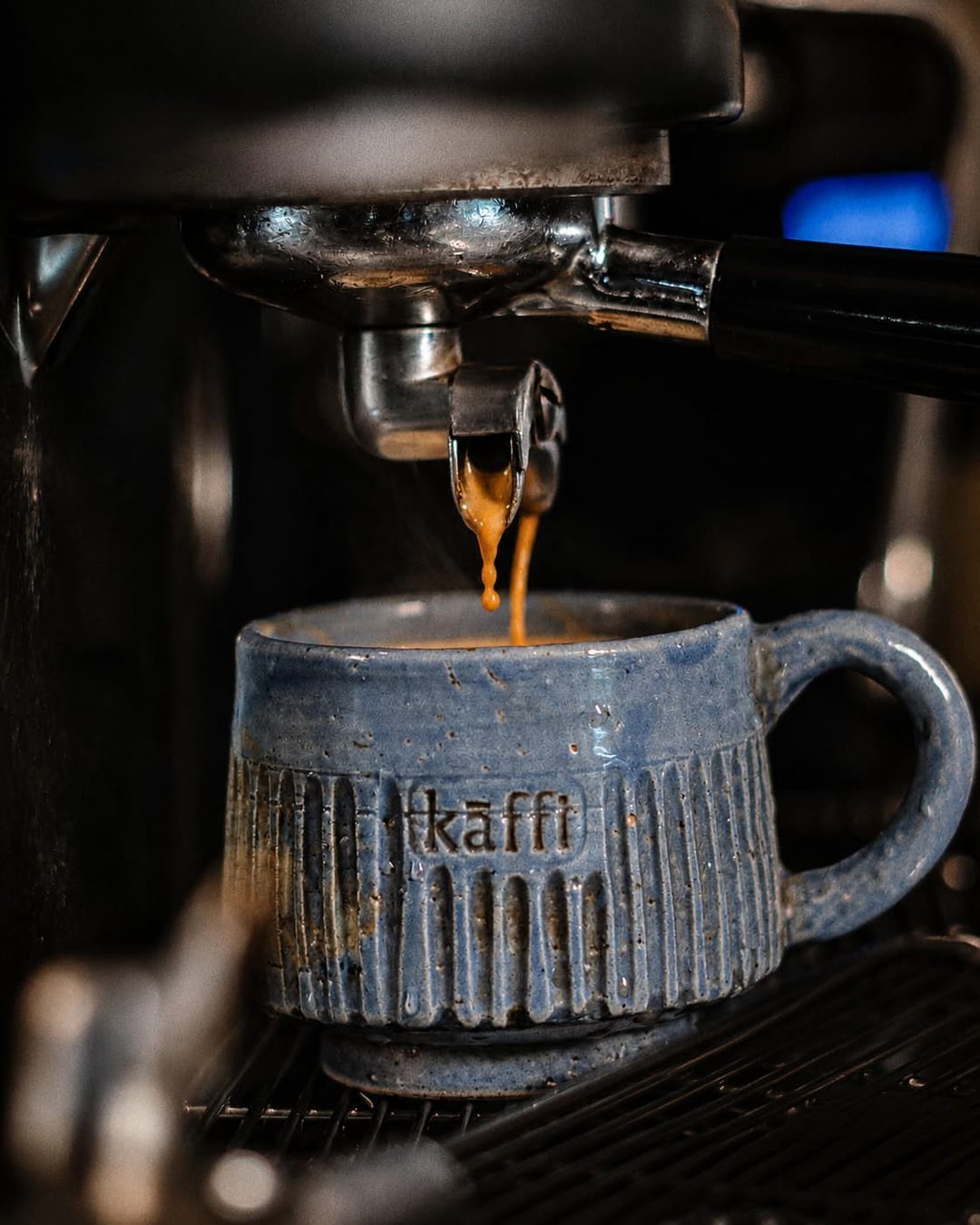 Espresso pouring from the portafilter into a blue hand-thrown cup