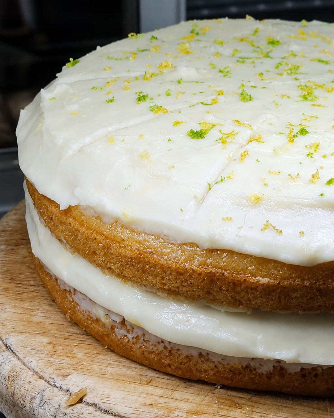 A lemon lime cake finished with zest, on a wooden board