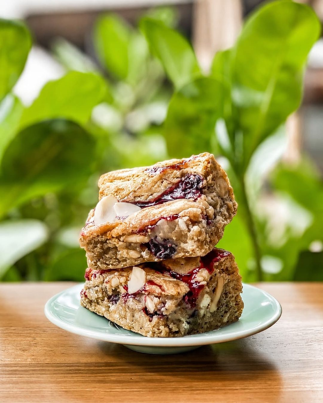 Two raspberry almond bars on a mint saucer, toasted almond slivers on top